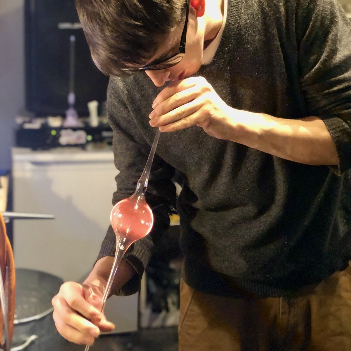 Glassblower blowing into a glass tube to create a bubble