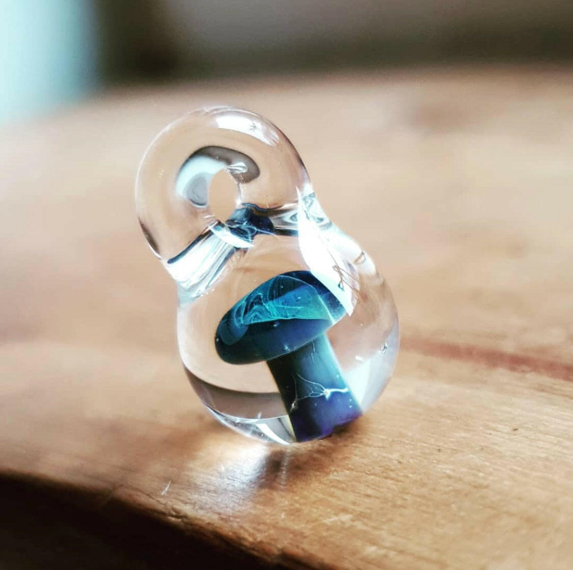 A borosilicate glass pendant with a blue mushroom design displayed on a wooden surface.